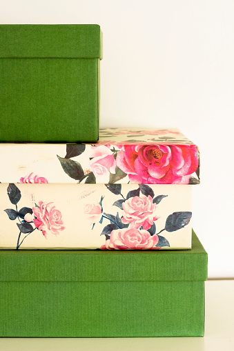 A DSLR photo of a stack of three cardboard boxes. The boxes at the top and the bottom are lined with green paper and the middle box is lined with a rose pattern paper. Crop view. 