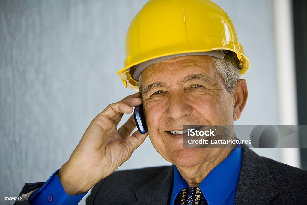 Close up of senior businessman wearing hardhat "Senior man wearing hardhat, talking on cellphone, looking at camera." 60-69 Years Stock Photo