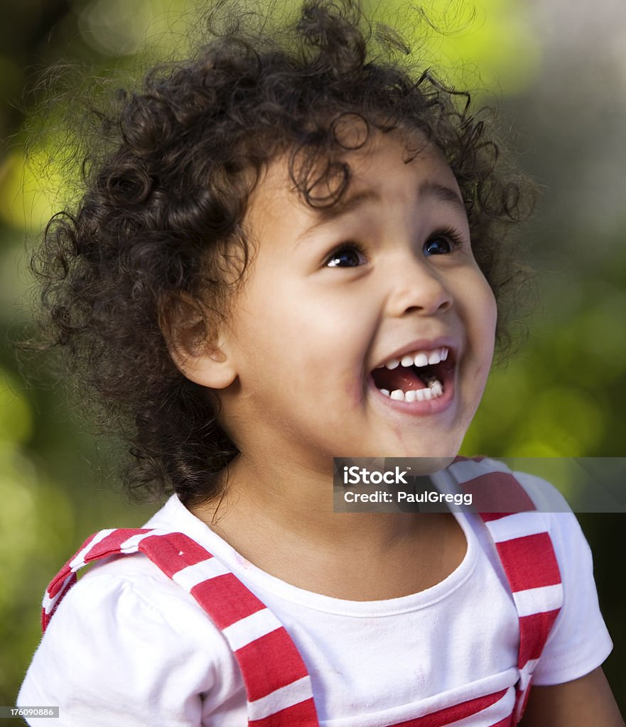 Portrait of a happy biracial African American child A young African American girl with a dirty face sitting in a park finding something amusing. Sunlight creating beautiful bokeh. Soft focus.Click African-American Ethnicity Stock Photo