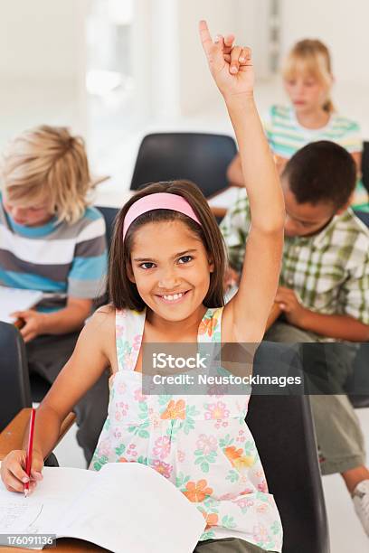 Intelligent Girl Raising Her Hand While Making Notes At Classroom Stock Photo - Download Image Now