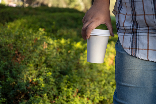 Strolling through the park, the girl carries a paper coffee cup, enjoying a leisurely walk in the serene surroundings.