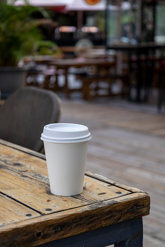 A paper coffee cup is perched on the table's edge in the cafe, adding a comforting touch to the scene.