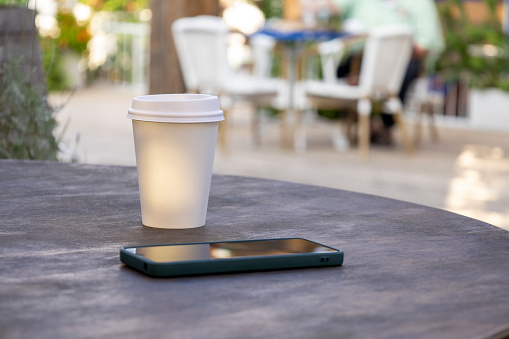 Positioned on the table, there's a phone and a paper cup of coffee, creating a mix of modern technology and a soothing beverage.