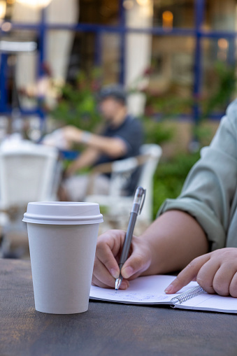 Within a comfortable coffee shop setting, the girl attentively jots down her thoughts and ideas, cultivating a peaceful and industrious environment.