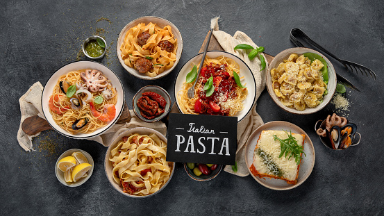 Pasta. Assortment of Italian pasta dishes, including spaghetti Bolognese, penne, tortellini, ravioli and others on a black background. Top view.