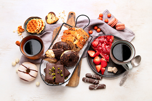 Cup of coffee with waffle, cookies, cake and dunut on light background. Hot drink and desserts. Top view.