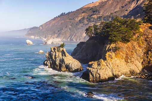 Scenic view of the rugged coastline of Big Sur with Santa Lucia Mountains and Big Creek Bridge along famous Highway 1 in beautiful golden evening light at sunset in summer, California Central Coast, USA