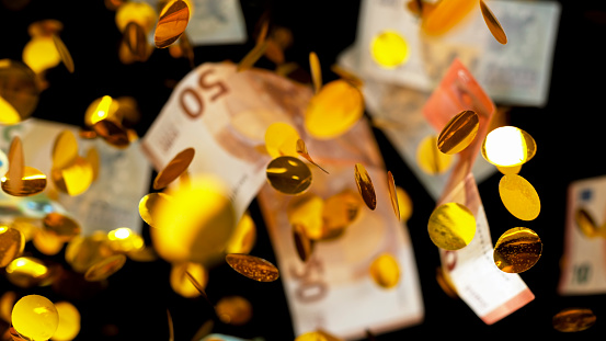 Close-up of banknotes and gold coins falling mid-air against black background.