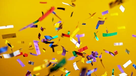 Close-up of multi coloured confetti flying mid-air against yellow background.