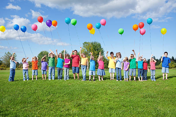 группа детей, стоя в очереди на воздушных шарах - child waiting in line in a row party стоковые фото и изображения
