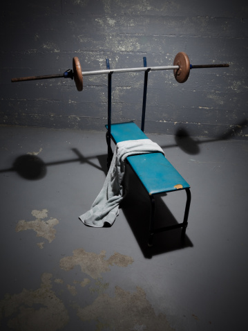A worn bench press in an old room. Single spot light with heavy vignetting.