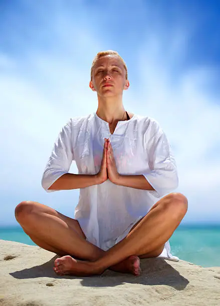 Young attractive woman exercise yoga at the beach rock, lotus position