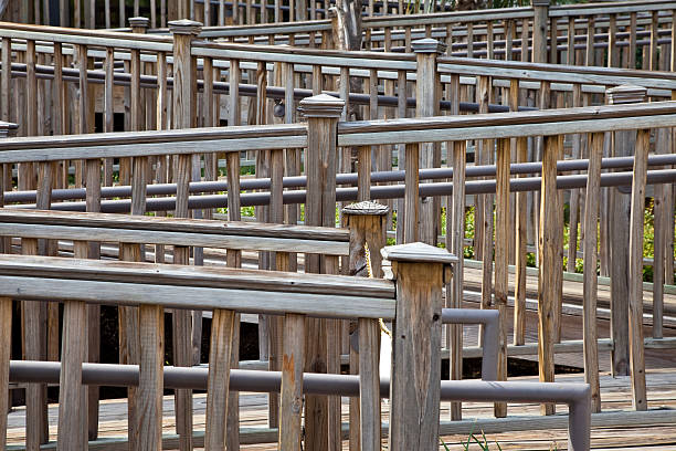 weathered wooden guardrails zig zagging along a walkway and deck. Some balusters are warped or loose. some wood has faded to a light gray or tan.