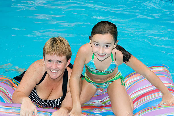Mother And Daughter On Inflatables In Outdoor Swimming Pool