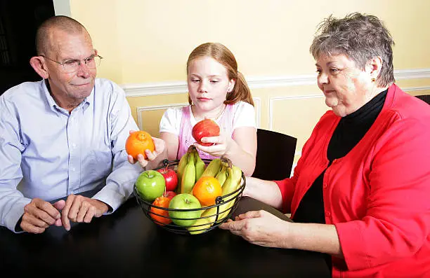 A little girl and her grandparents with a bowl of fruit