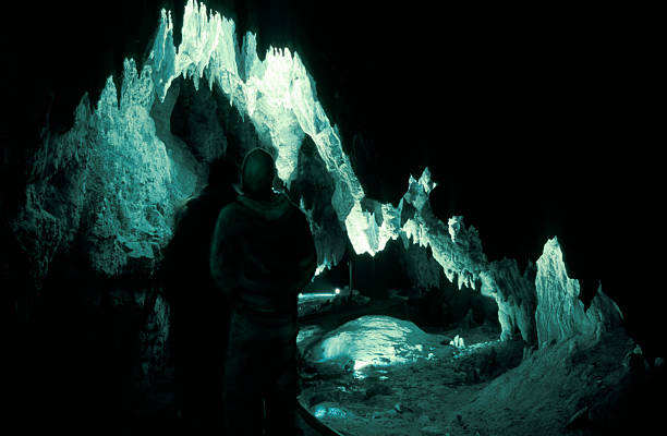illuminated stalactite cave Inside of a stalactite cave in Waitomo (New Zealand). Silhouettes of two visitors framed by stalactites in front of the illuminated cave. Toned. waitomo caves stock pictures, royalty-free photos & images