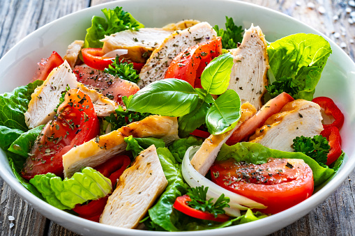 Caesar style salad  - fresh vegetables with grilled sliced chicken breast on wooden table