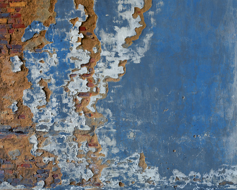 A damaged brick wall, its surface bearing the traces of time, is the focal point. Once painted in a vivid shade of blue, the paint has peeled off, revealing the rugged character of the underlying bricks. This abstract composition captures the beauty in imperfection and the artistry of decay.
