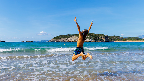 Happy summer holiday- young child jumping in the air on the beach