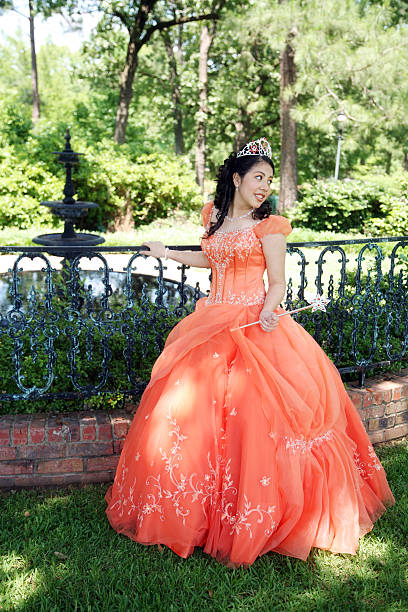 Young lady posing in an orange gown and a tiara Young teen wearing a beautiful gown on her 15th birthday. quinceanera stock pictures, royalty-free photos & images