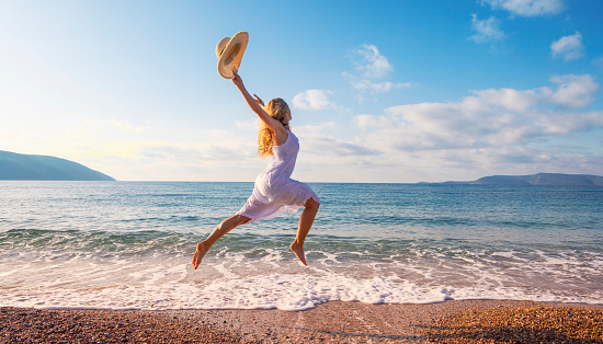 Girl jumping. Woman with white dress and hat jump on the beach