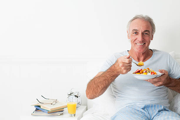 Happy senior man eating breakfest Happy senior man eating breakfest in his sunny bedroom. cerial stock pictures, royalty-free photos & images