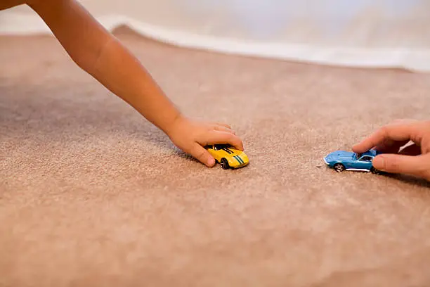 A child and an adult play with toy cars on a carpeted floor.