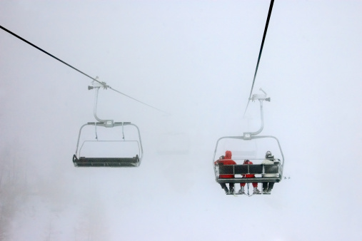 Family is traveling on a ski lift in foggy weather. Grainy image.