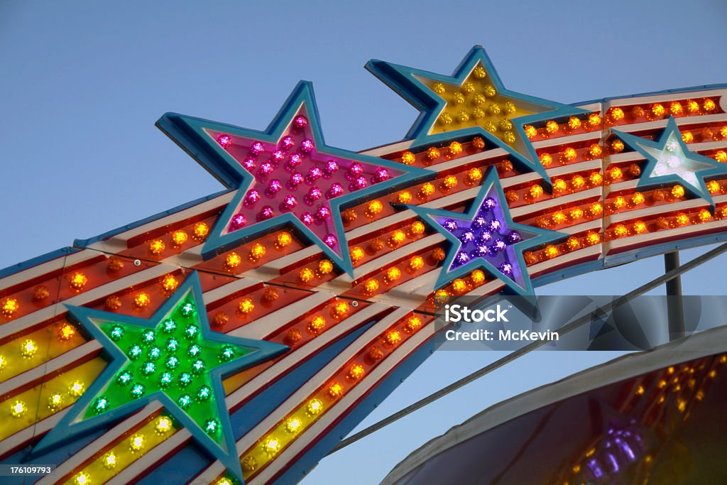 star lights in an amusement park sign Detail of a marquee at an amusement park with multicolored stars inlaid into the rays of an arch suggesting a rainbow. The time of day is dusk with the chasing clear incandescent bulbs beginning to glow brighly. Amusement Arcade Stock Photo