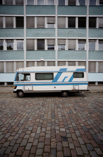 Old caravan in front of and old broken down apartment building. The apartments look like subsidized housing projects. The mood of the image is very grim and depressing.