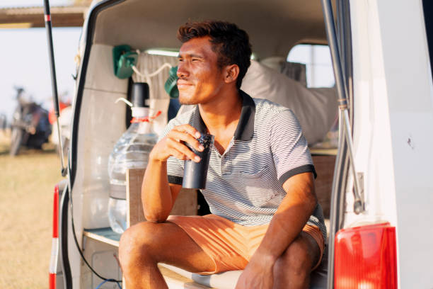 istock Indonesian Man Sitting Enjoying Drinks at the Back of a Van at Sunset 1761105251