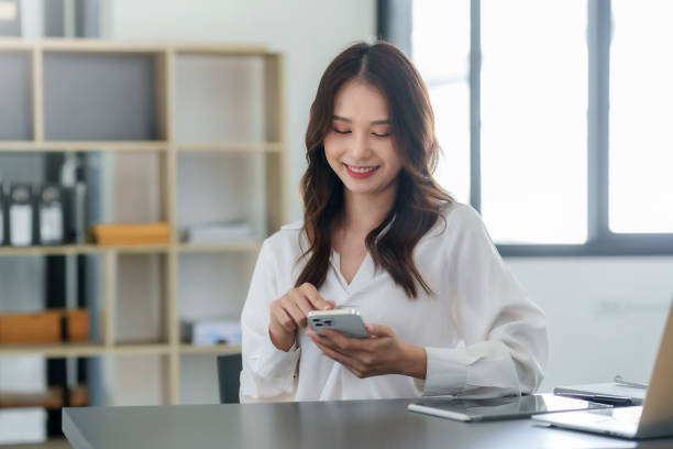istock Smiling Asian businesswoman using smartphone at office. 1761109527