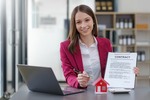 Female real estate agent presenting details of a house for sale and  contract signing document.