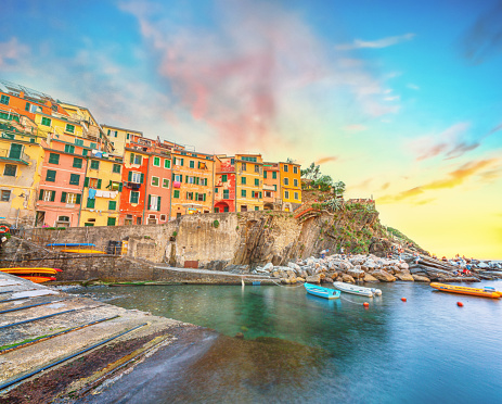 As the sun dips below the horizon, Riomaggiore, a charming fishing village in Cinque Terre, Italy, comes alive with a delightful display of colorful houses. The sky is adorned with hues of yellow and blue, casting a serene and vibrant atmosphere over the Ligurian Sea. It's a captivating scene that beckons you to immerse yourself in its enchanting beauty.