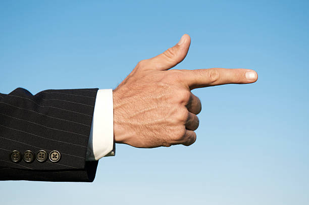 Businessman in dark pinstripe suit points his hand in soft blue sky