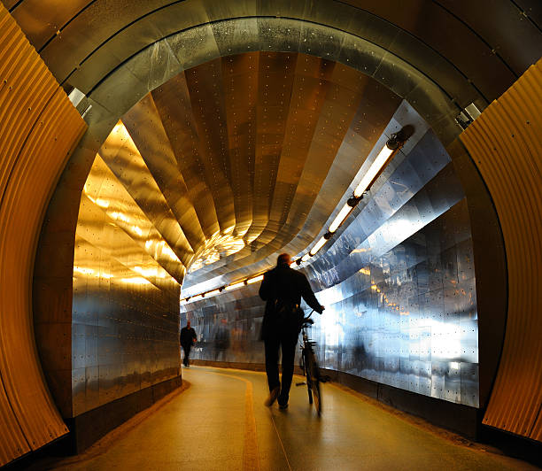 Light at the end of the tunnel. Silhouettes of walking men / persons and bike. Bright daylight reflected from metal walls.See also: