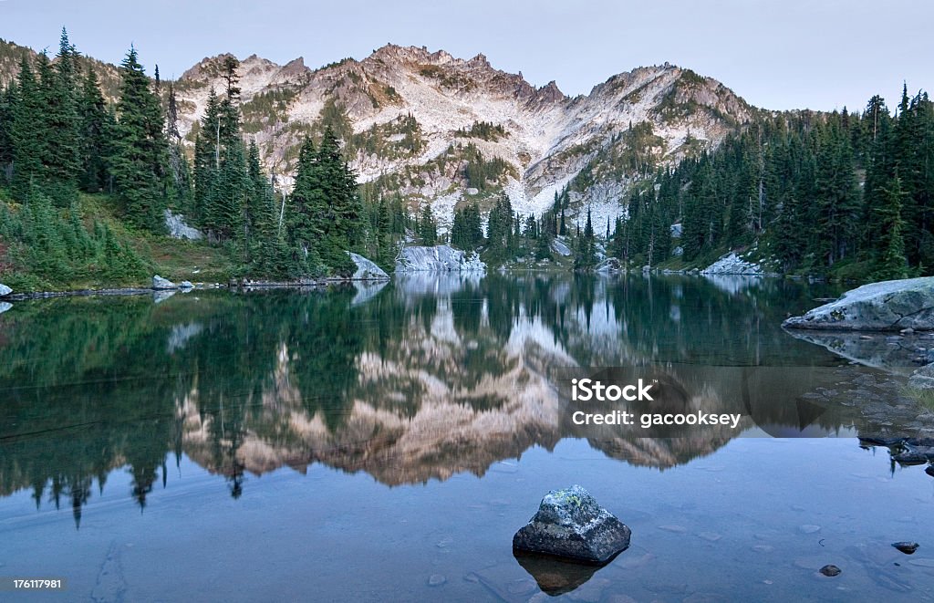 Mountain reflection in alpine lake Reflection of rugged mountain over still lake.  Late evening light.  Alpine Lakes Wilderness Stock Photo