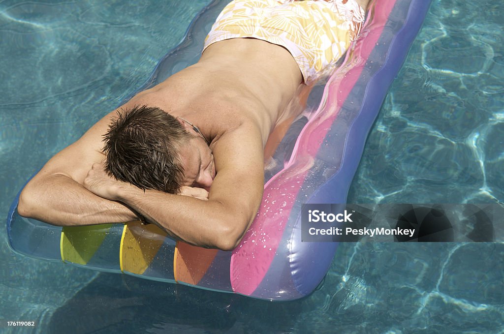 Guy Floats in Pool on Rainbow Lilo Guy cradles his head into his arms floating on a rainbow pool raft in sparkling blue water Adult Stock Photo