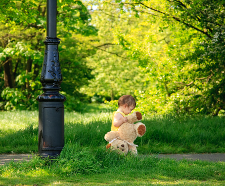 Toddler baby girl of 14 months age walking with teddy bear in a wooded park