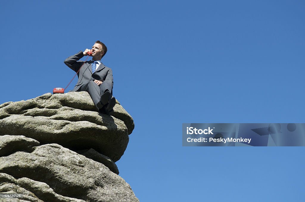 Biznesmen siedzi na zewnątrz górnej części Rock rozmawia przez telefon - Zbiór zdjęć royalty-free (Góra)