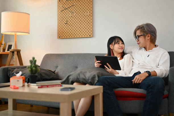 istock Happy young couple using digital tablet while relaxing in living room together 1761215253