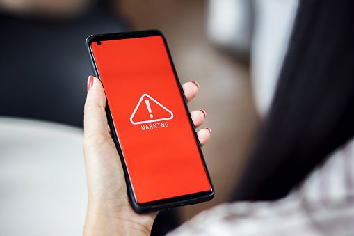 woman using smartphone with warning triangle showing a system error. Concepts of system maintenance, security, anti-virus, and anti-hacking access to critical data.