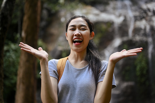 Cheerful young woman backpacker enjoying nature with waterfall in background.