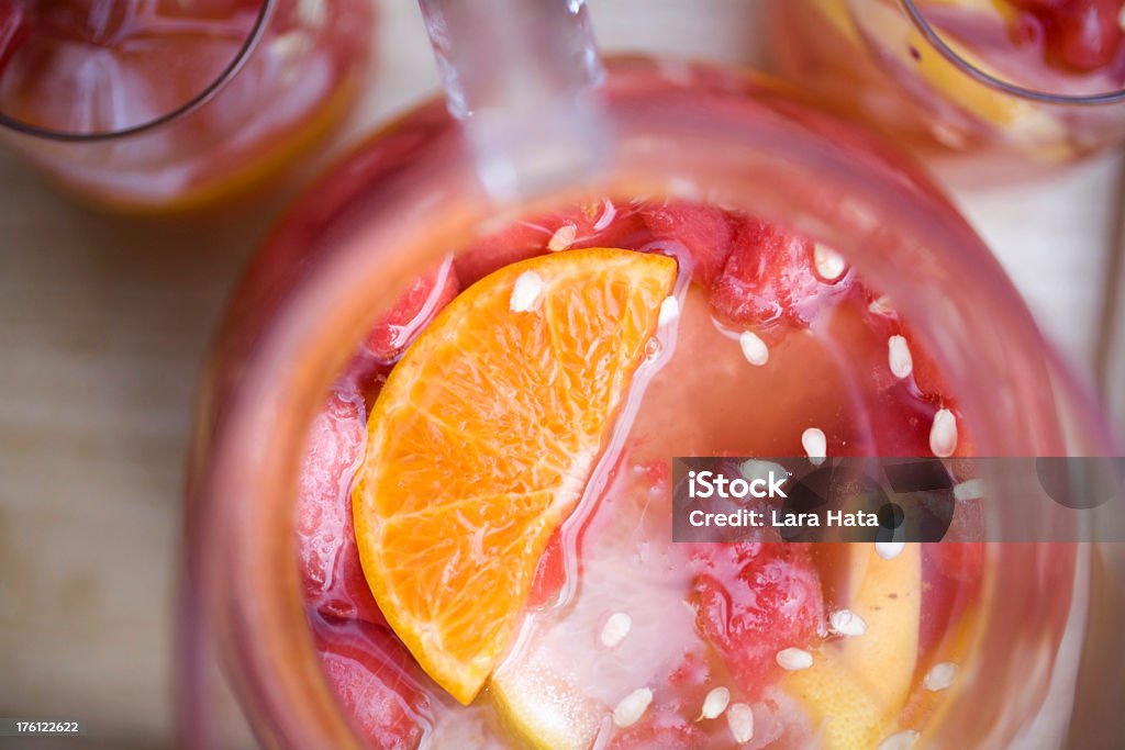 Top view of red sangria pitcher and glasses with orange Watermelon, tangerine and grapefruit sangria made with white wine in a large glass pitcher on an outdoor patio table.  Close-up shot of the pitcher showing the sliced fruit sections, seeds and ice cubes. Grapefruit Stock Photo