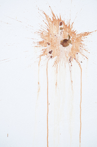 Juicy orange splat dirty stain with particles on white wall