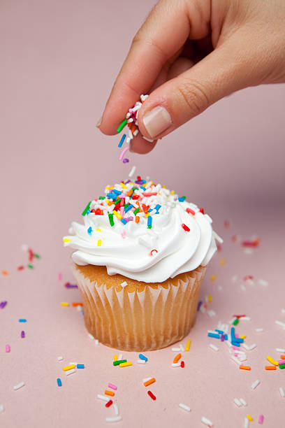 saupoudrer confettis en sucre sur cupcake - saupoudrer photos et images de collection