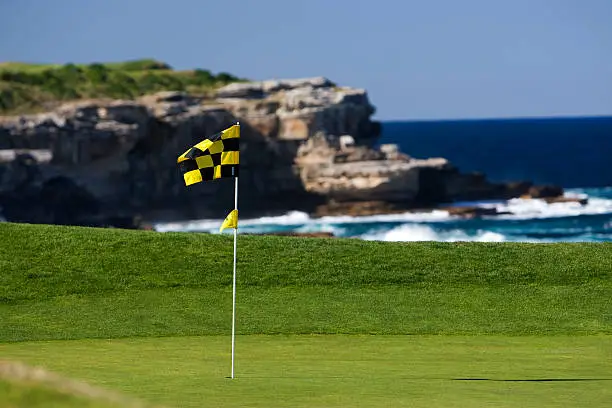 A golf flag blows in the wind on a beautiful golf course by the ocean.