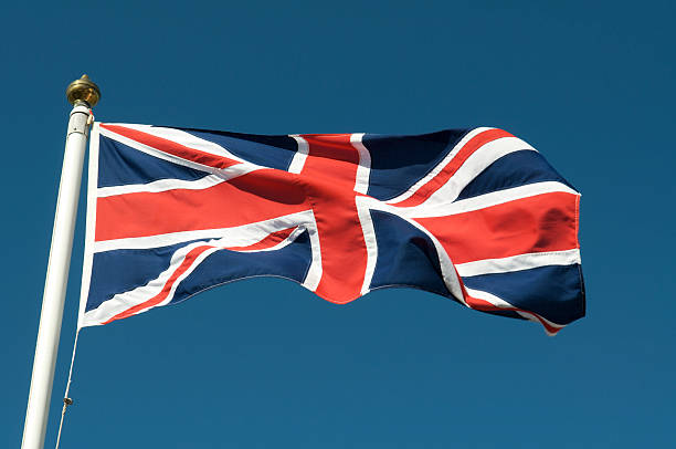 istock Union Jack Fluttering on Flag Pole in Blue Sky 176126325