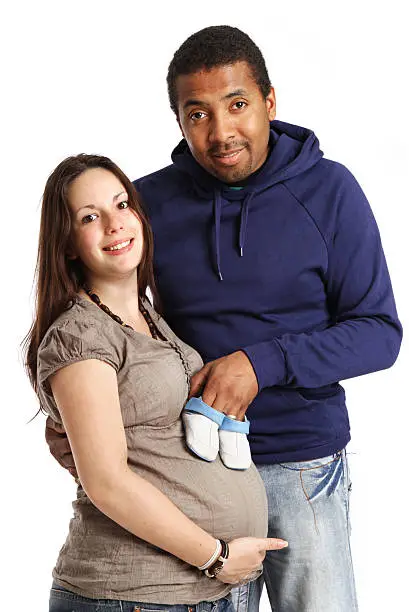 A mixed race couple expecting their first baby. Posing with little babyshoes on her big belly...