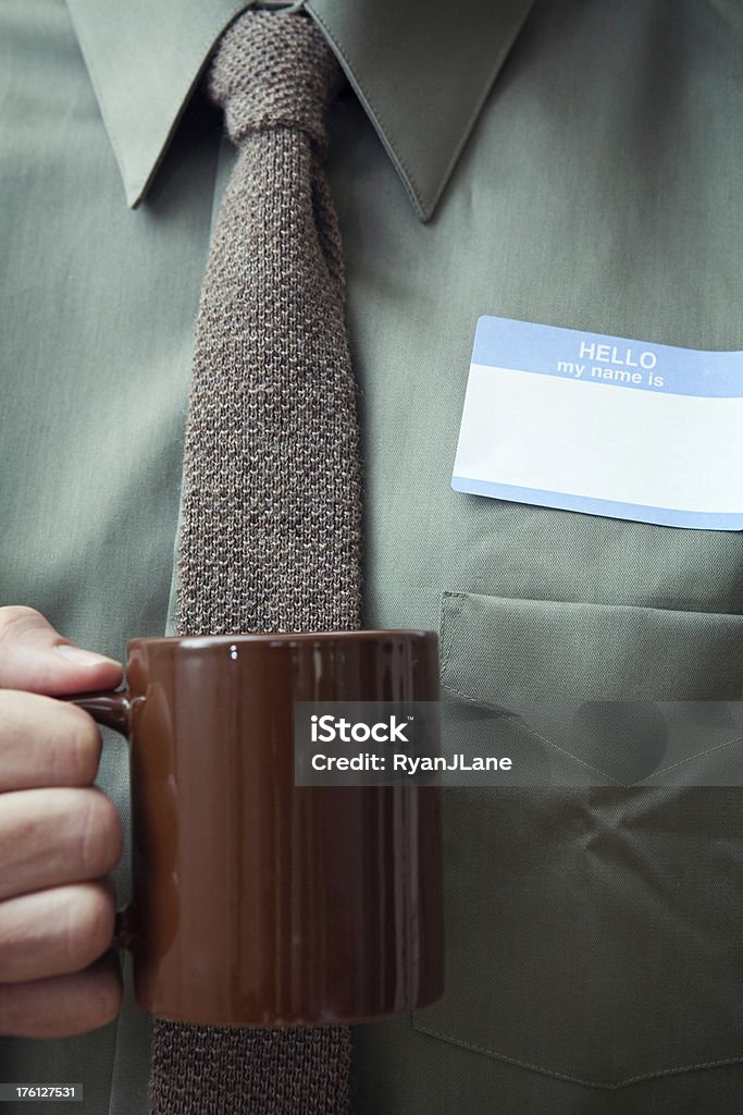 Hello My Name Is A close up shot of a man in stylish business clothes holding a brown mug with a identification name tag stuck on his shirt.  Vertical with copy space. Identity Stock Photo